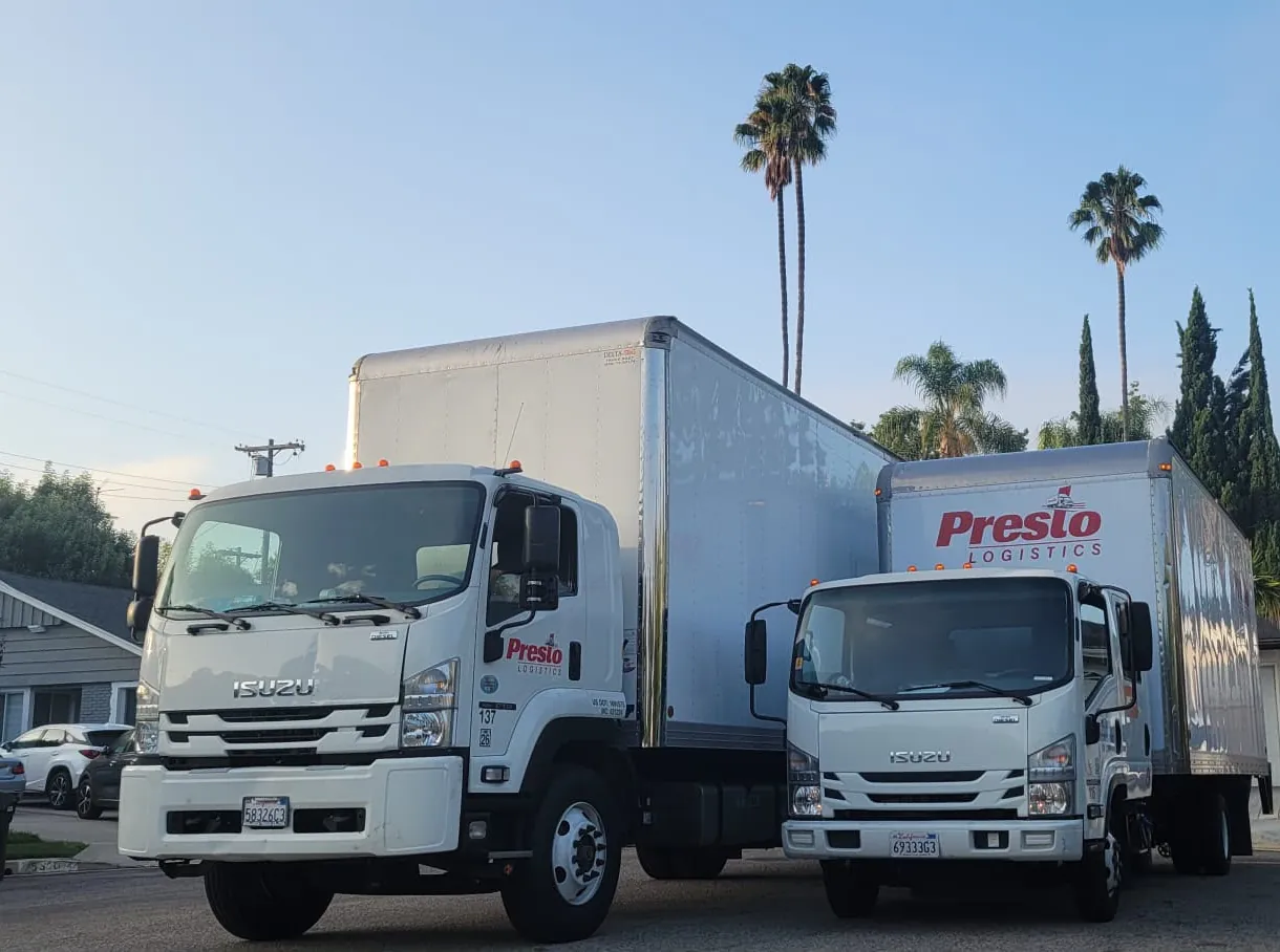 Two Presto Logistics moving trucks parked under palm trees